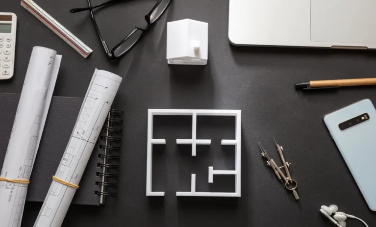 Mesa de trabajo con planos y maqueta de distribución de una vivienda