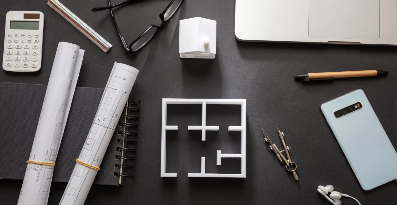 Mesa de trabajo con planos y maqueta de distribución de una vivienda